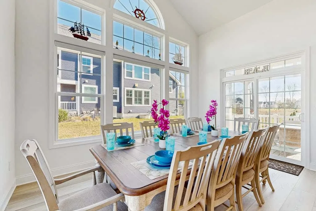 A bright dining room with a long table set beside large windows.
