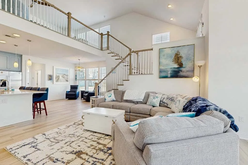 A bright open-plan living area with seating, a rug, and a staircase.
