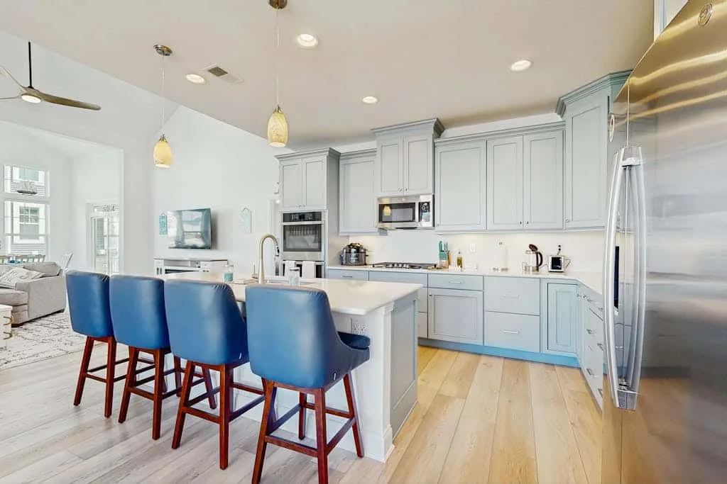 Una cocina luminosa cuenta con una isla central, asientos azules y gabinetes claros.