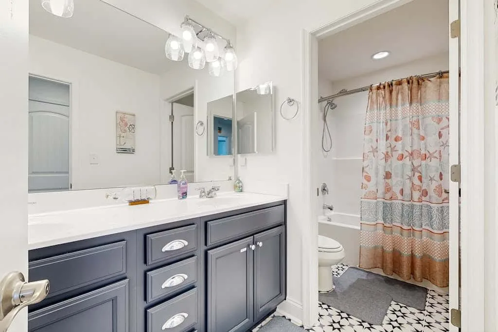 Un mueble de baño con un lavabo amplio está junto a una bañera con cortina estampada.