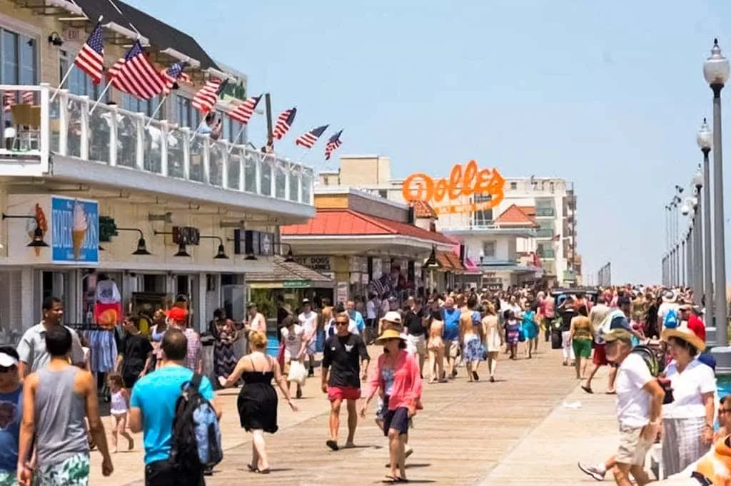 Un concurrido paseo marítimo con tiendas y banderas estadounidenses.
