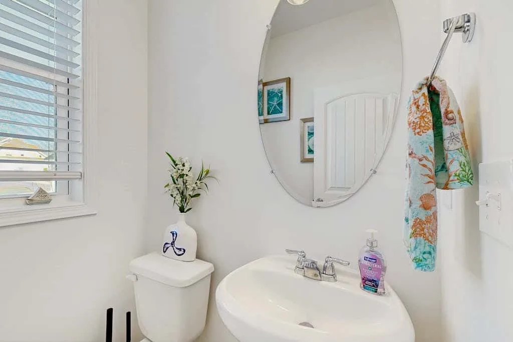 Un baño luminoso con lavabo, espejo ovalado y ventana con persianas.