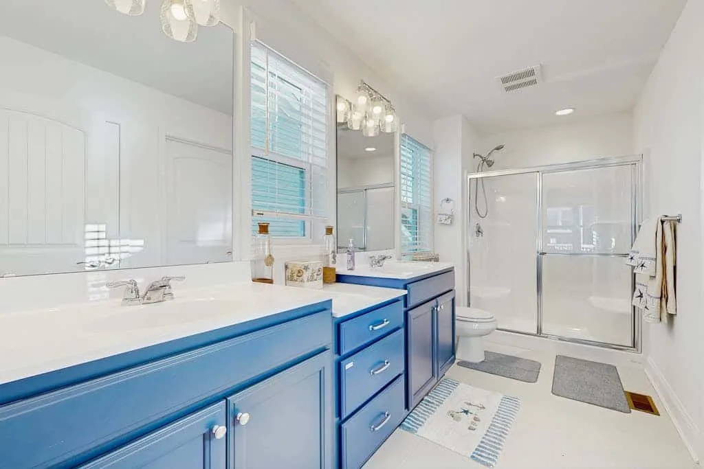 Un baño luminoso con gabinetes azules y una ducha de vidrio.
