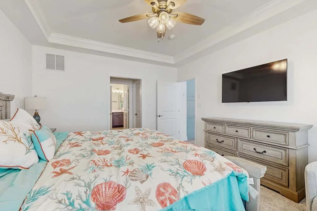 Un dormitorio con una colcha estampada, una cómoda y un televisor en la pared.