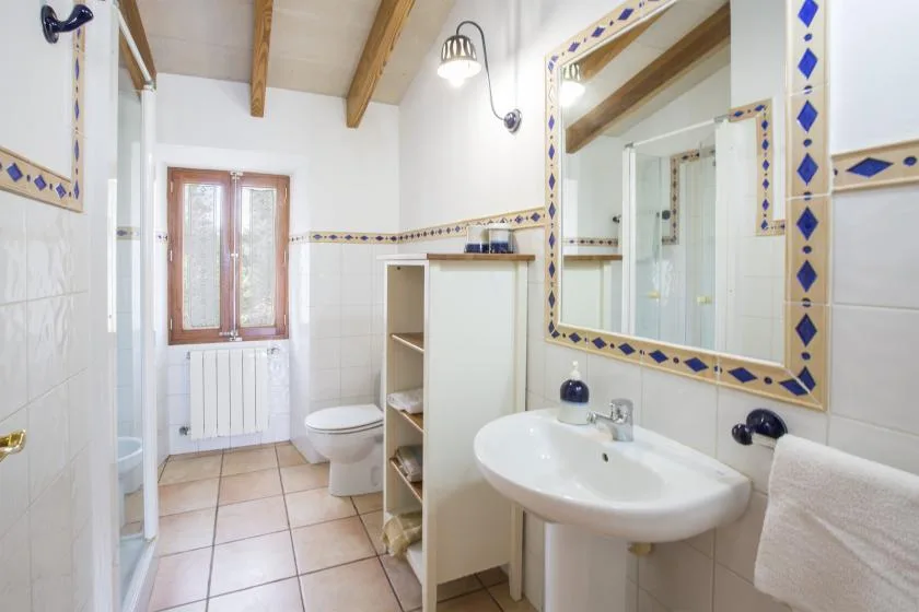 A tiled bathroom with a sink, toilet, and window.
