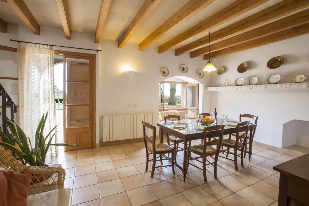 A dining area with a wooden table and chairs beneath exposed ceiling beams.