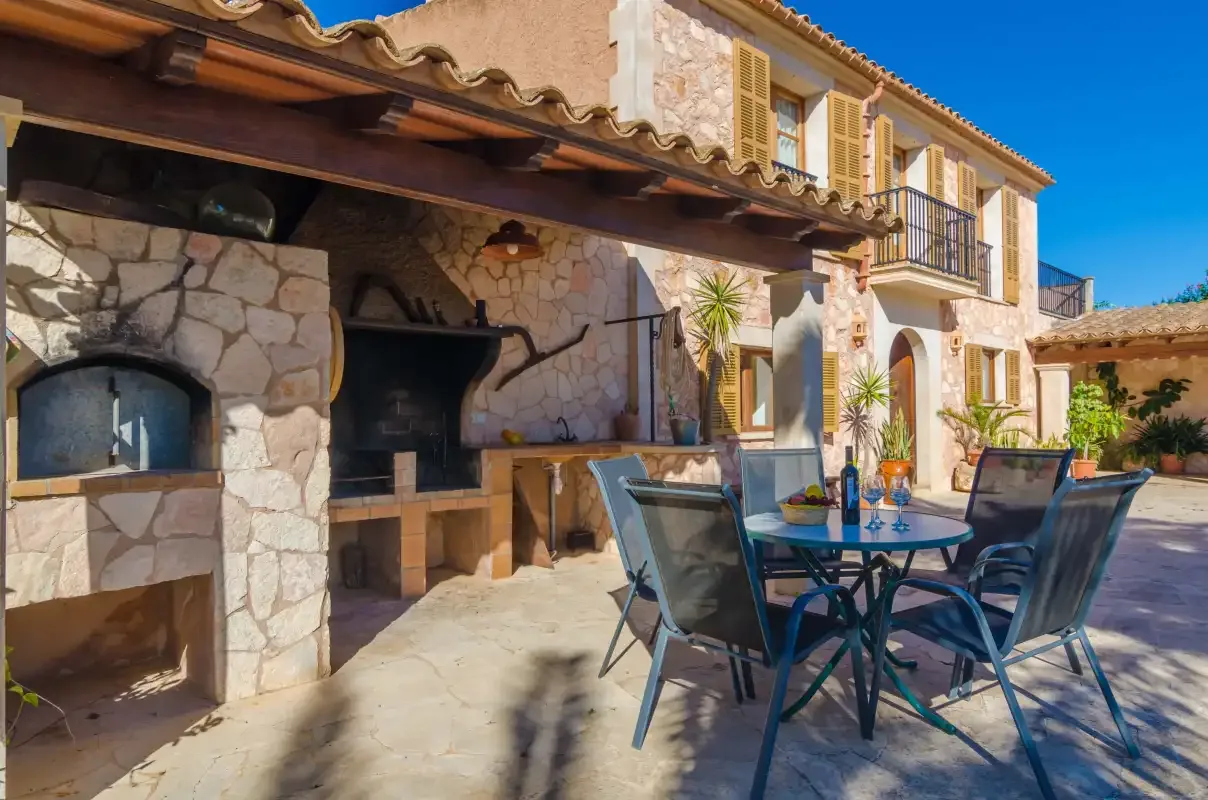 A stone patio with an outdoor barbecue and a table with seating.