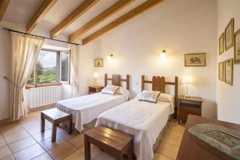 A bedroom with two beds, wooden bedside tables, and a window with curtains.