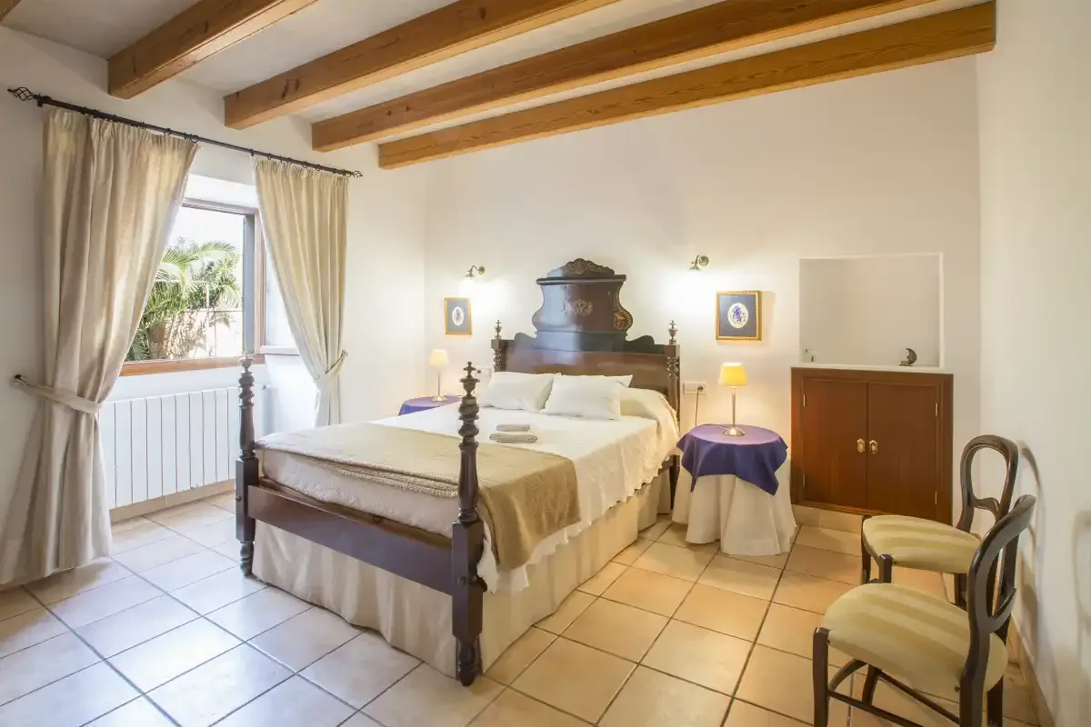 A bright bedroom with a large bed, exposed ceiling beams, and a window.