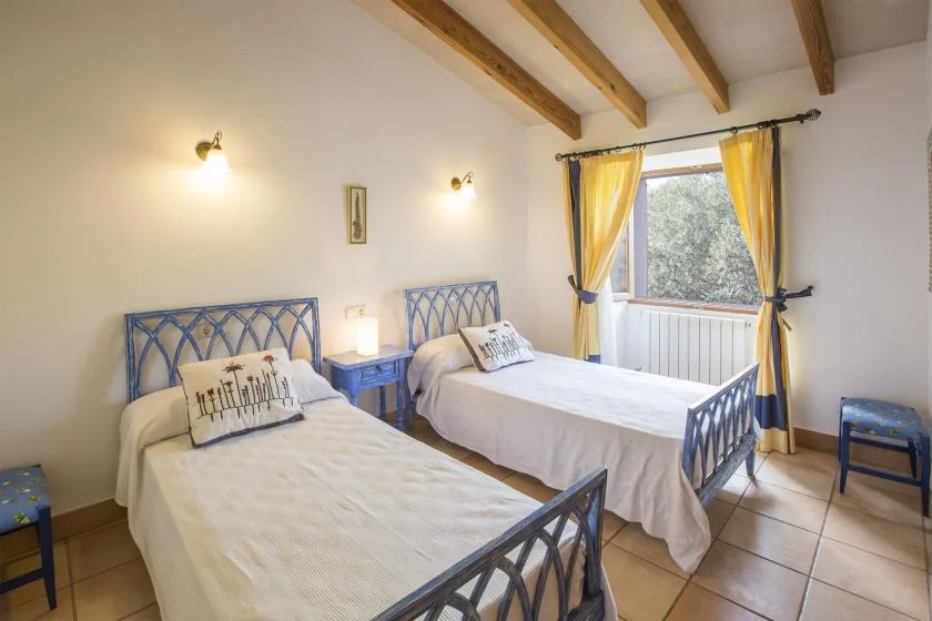 A bedroom with two beds, blue metal frames, and yellow curtains.