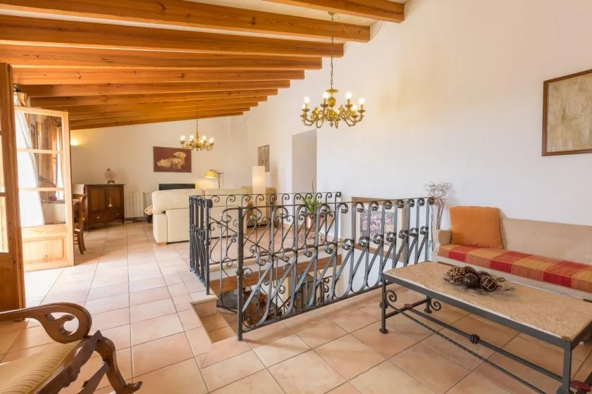 A bright sitting area with exposed wooden ceiling beams and a wrought-iron railing.
