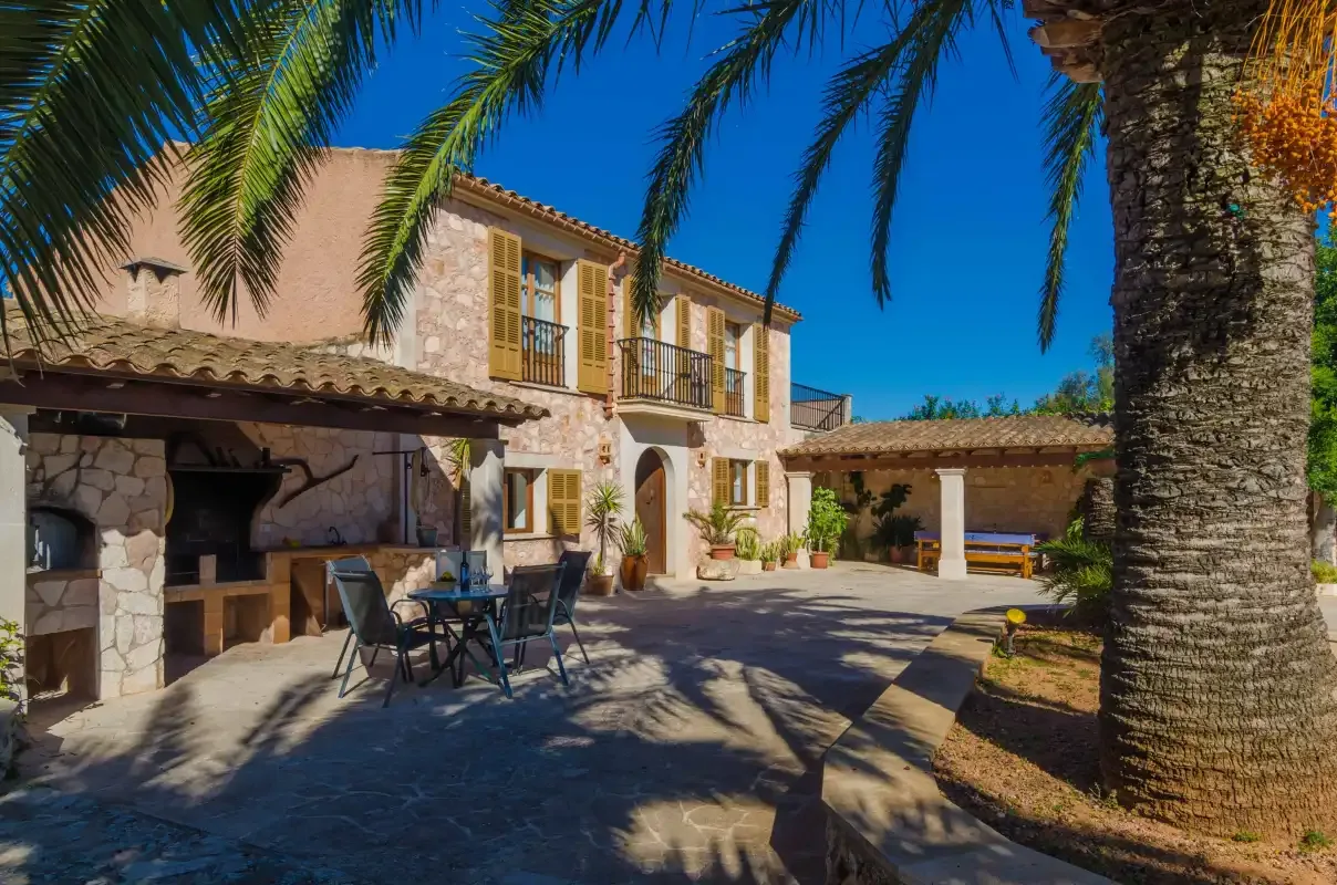 A stone house with an outdoor dining area beneath palm trees.