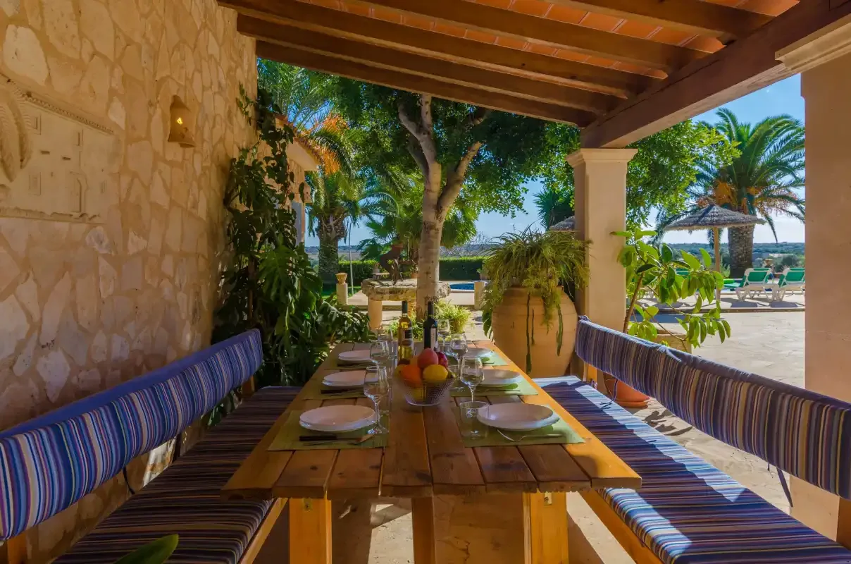 A covered outdoor dining area with a long wooden table and striped seating.