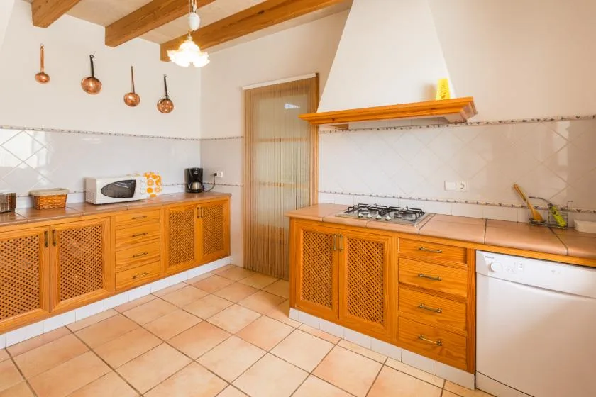 A kitchen with wooden cabinets, a cooktop, and a tiled floor.