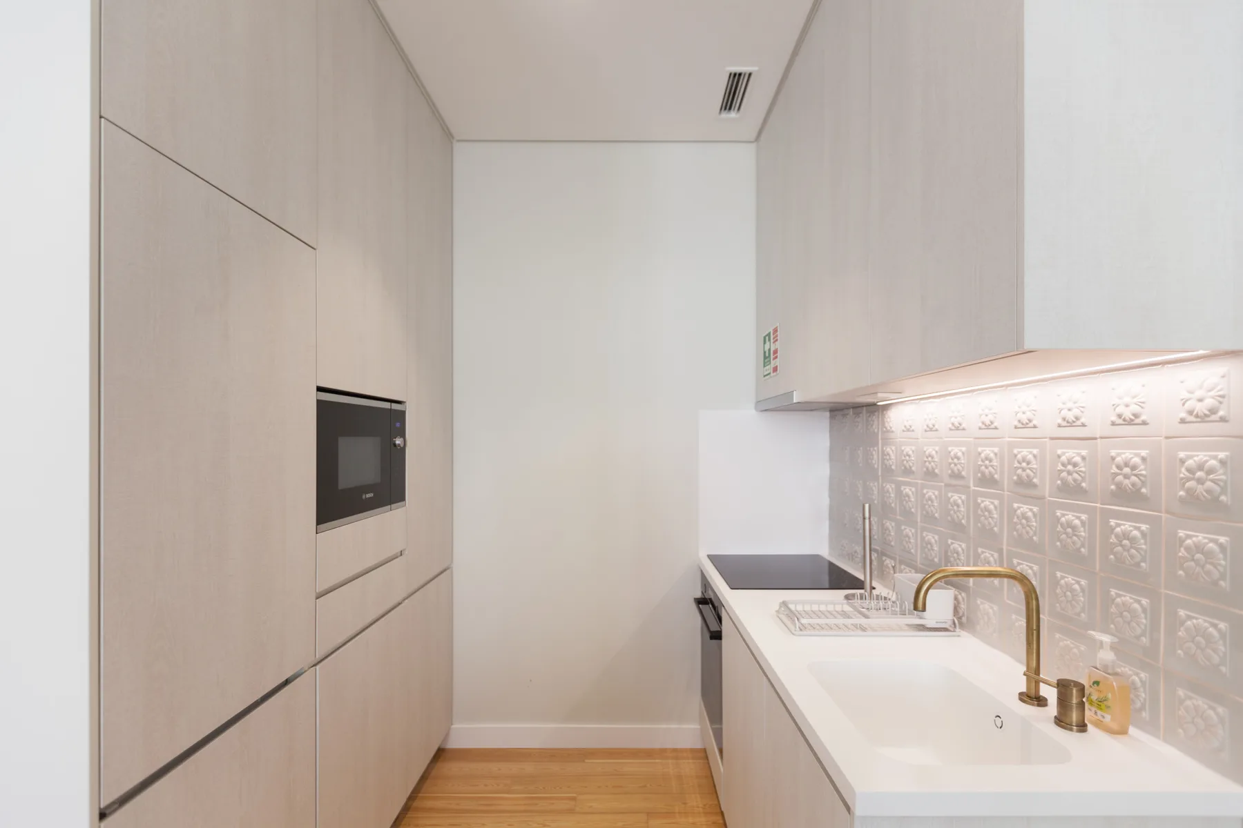 Una cocina compacta con horno integrado, fregadero y pared de azulejos.