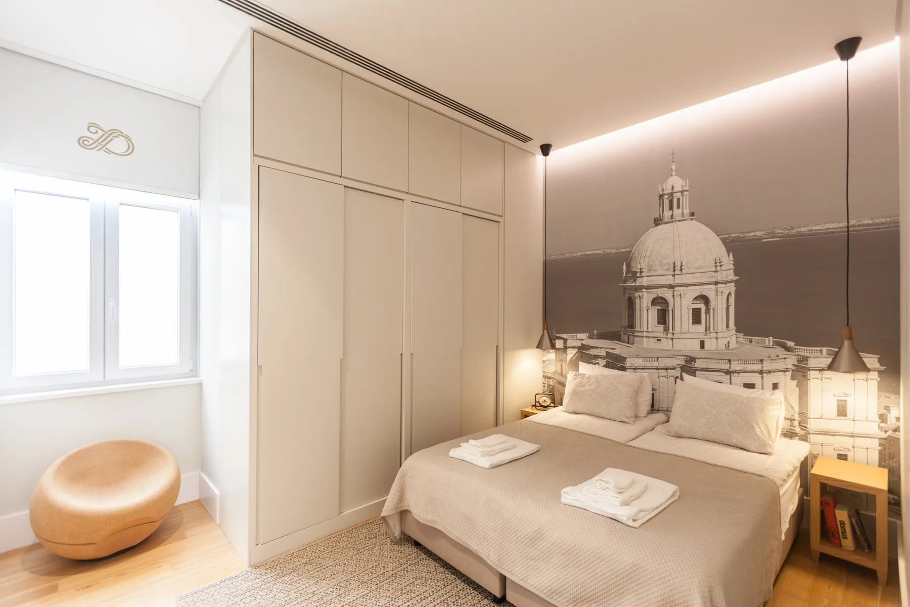 A bedroom with a neatly made bed and a large architectural mural behind it.