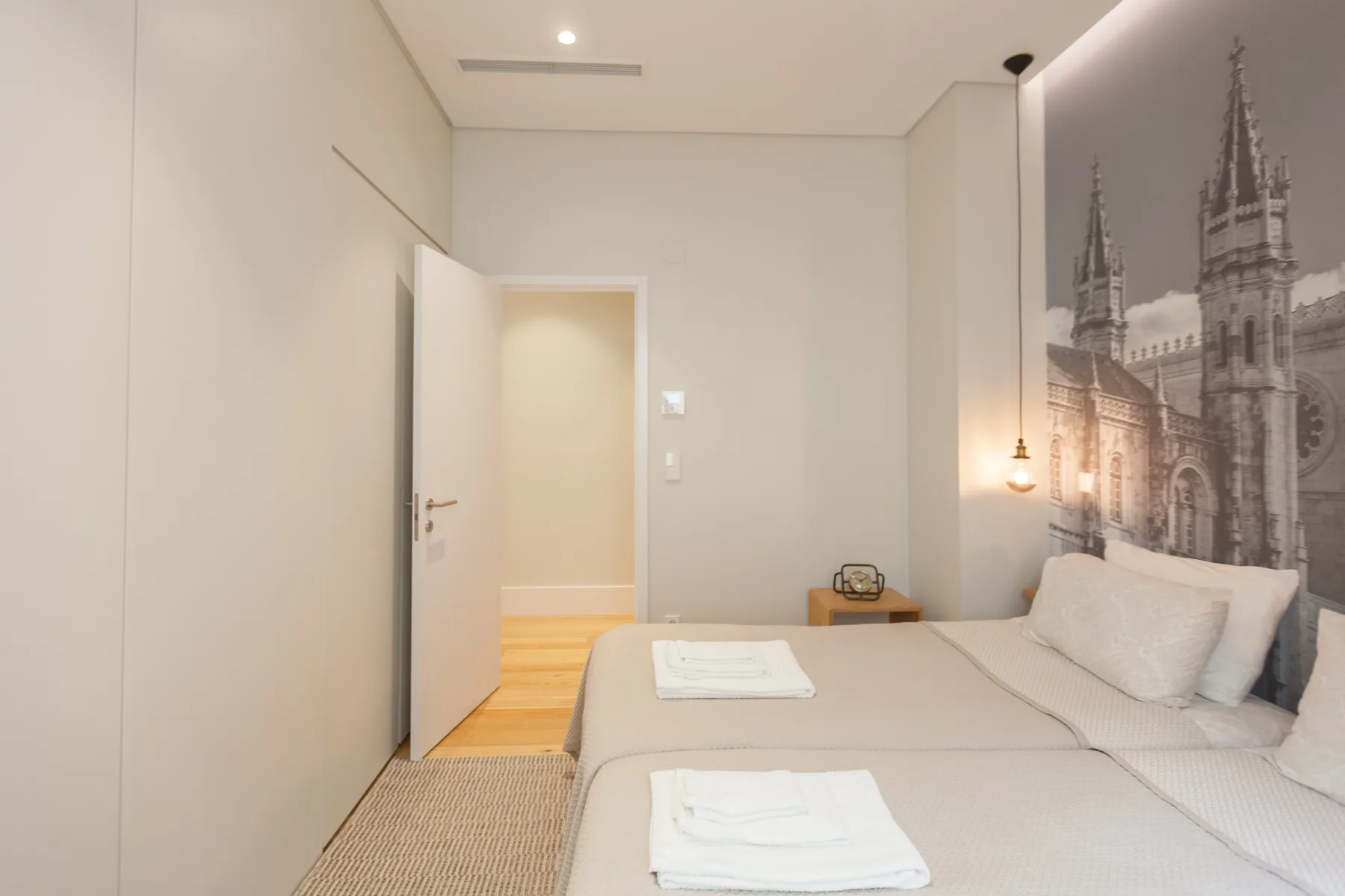 A bedroom with a neatly made bed and a large architectural wall mural.