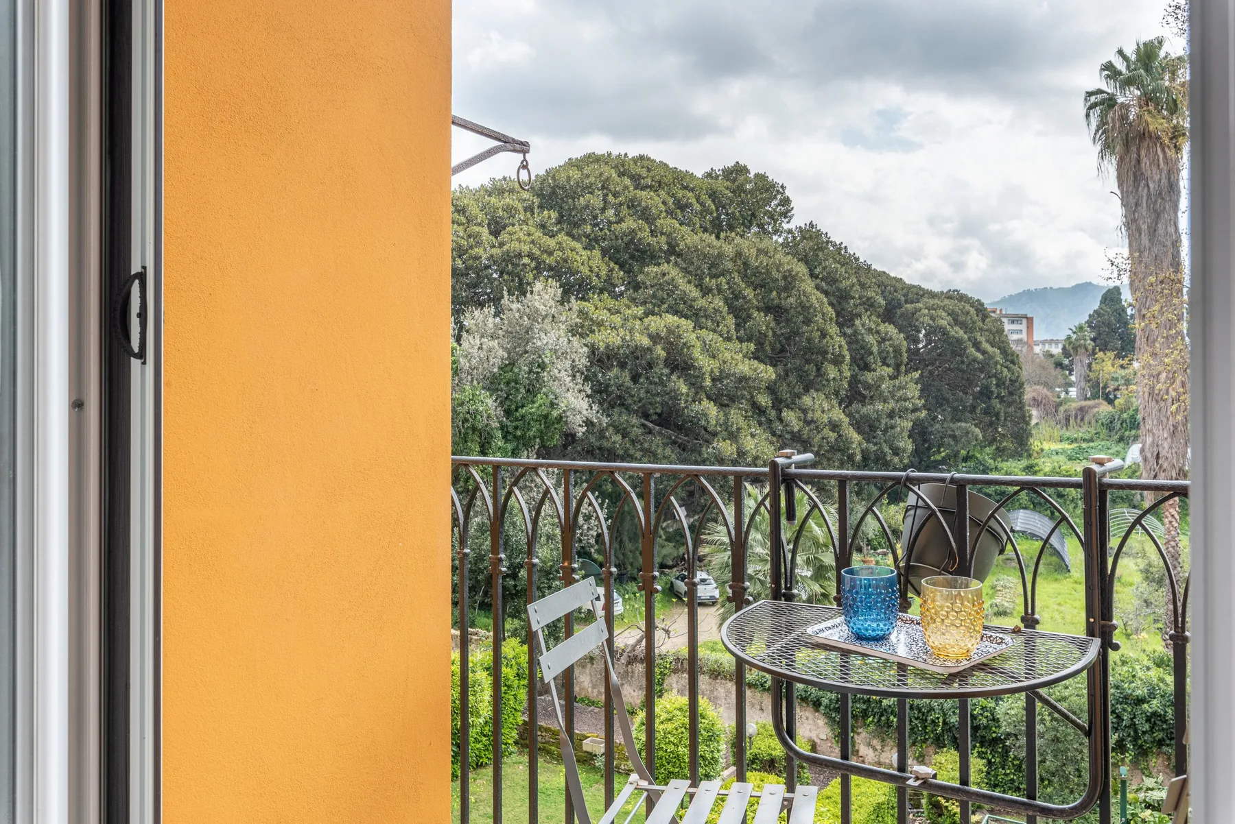 A balcony seating area overlooks leafy gardens and trees.