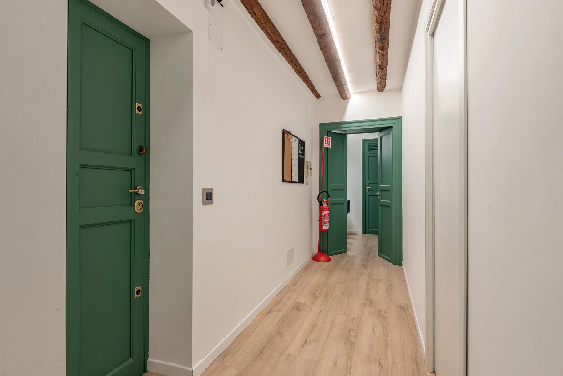 A narrow hallway with green doors and exposed ceiling beams.