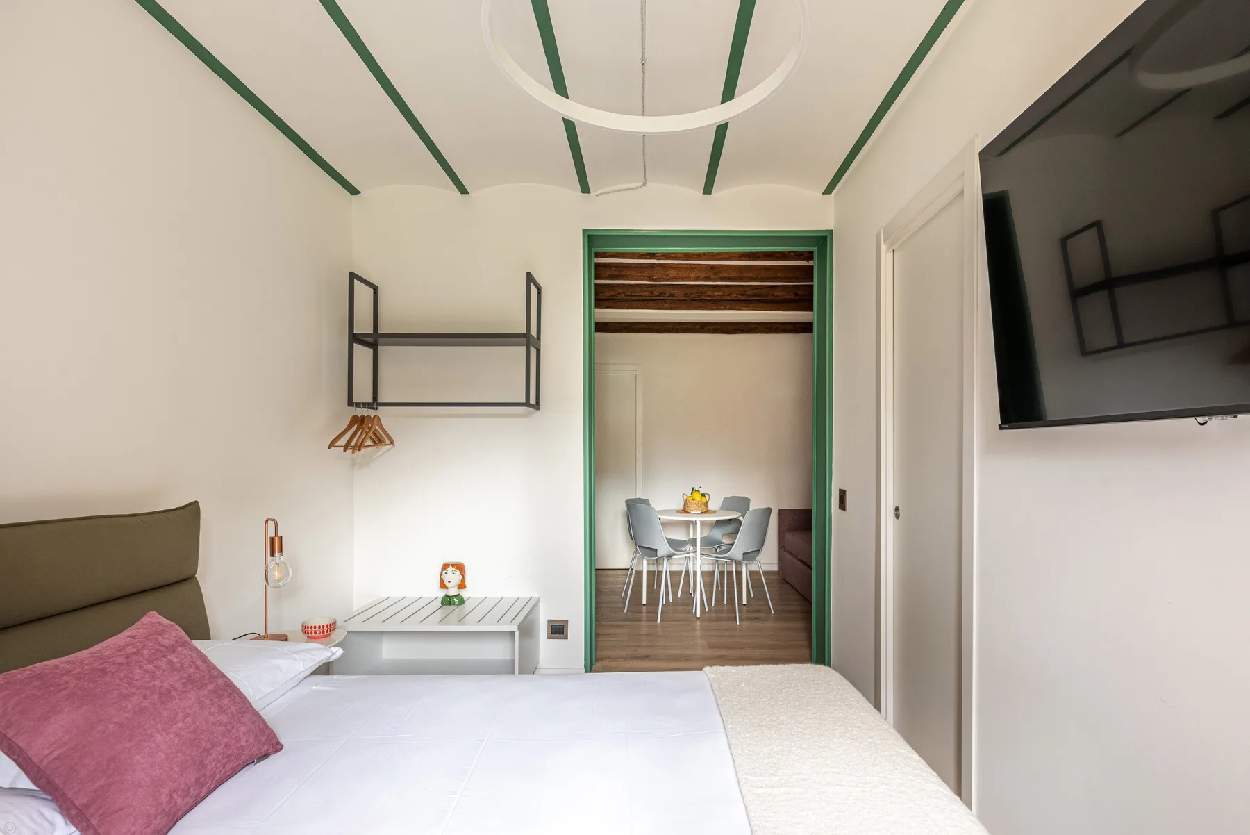 A bedroom with a bed, wall-mounted television, and an open doorway to a dining area.