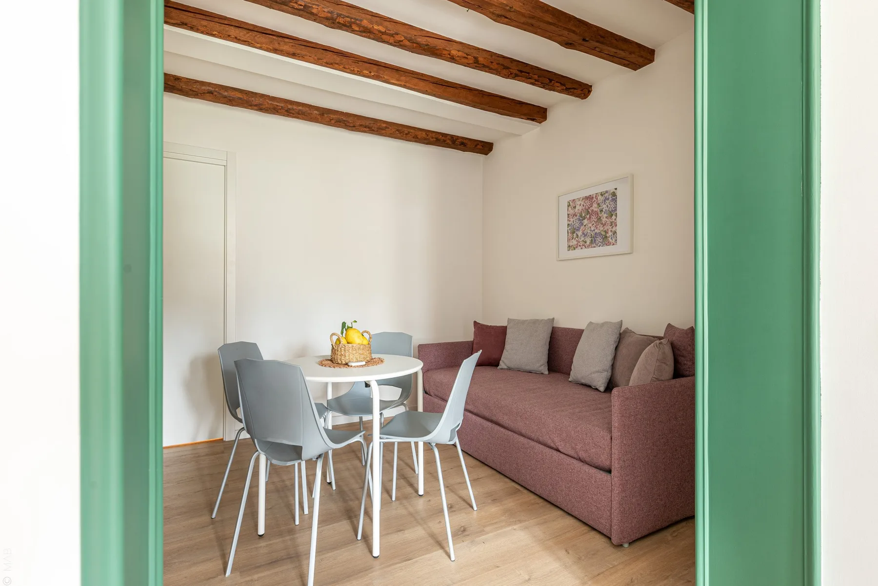 A dining and seating area with a round table, chairs, and a mauve sofa.