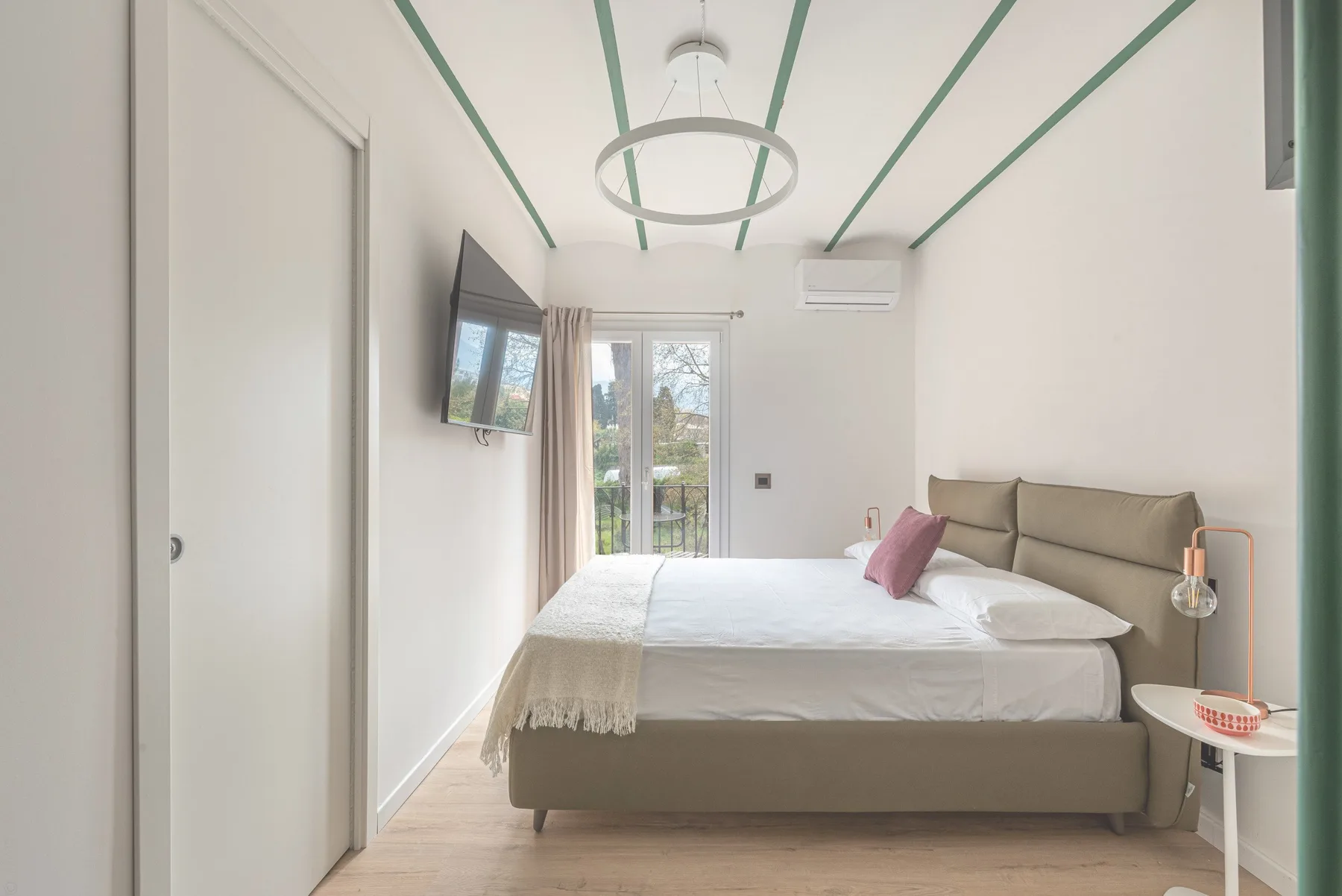 A bright bedroom with a neatly made bed and glass doors to a balcony.