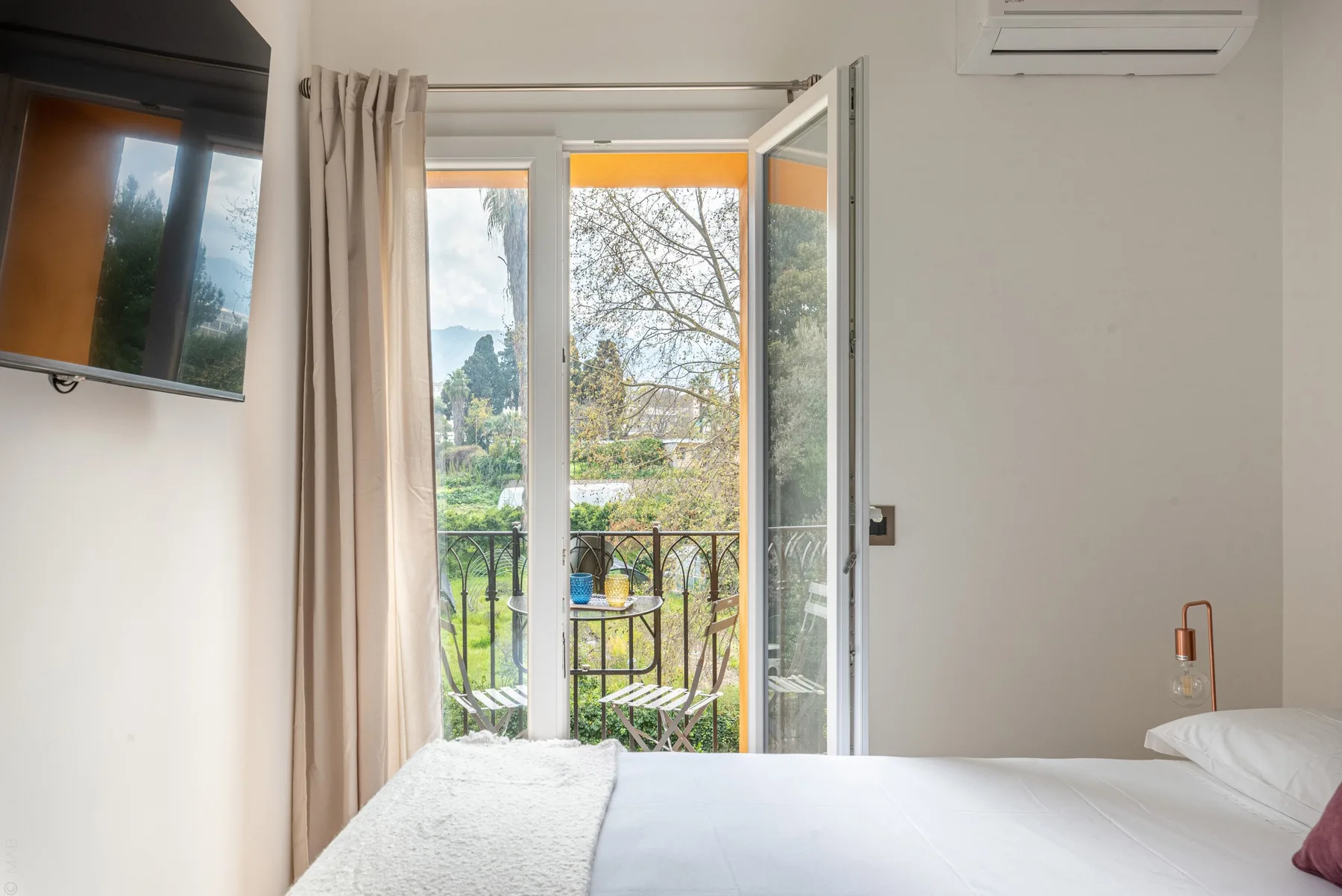 Un dormitorio con la puerta del balcón abierta y vistas a la vegetación exterior.