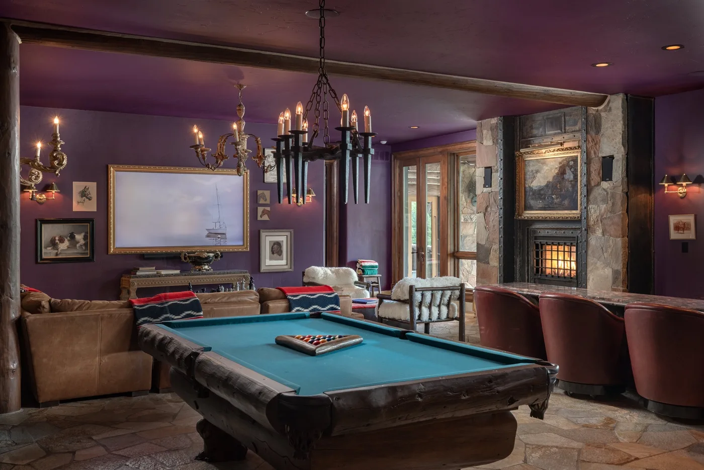 A billiards room with a pool table, seating, and a stone fireplace.