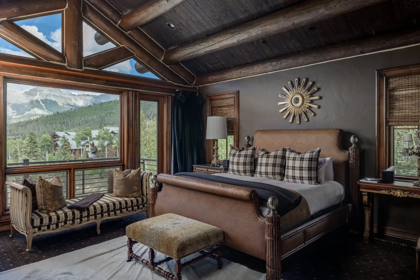 A bedroom with a large bed and seating beside windows overlooking a mountain landscape.