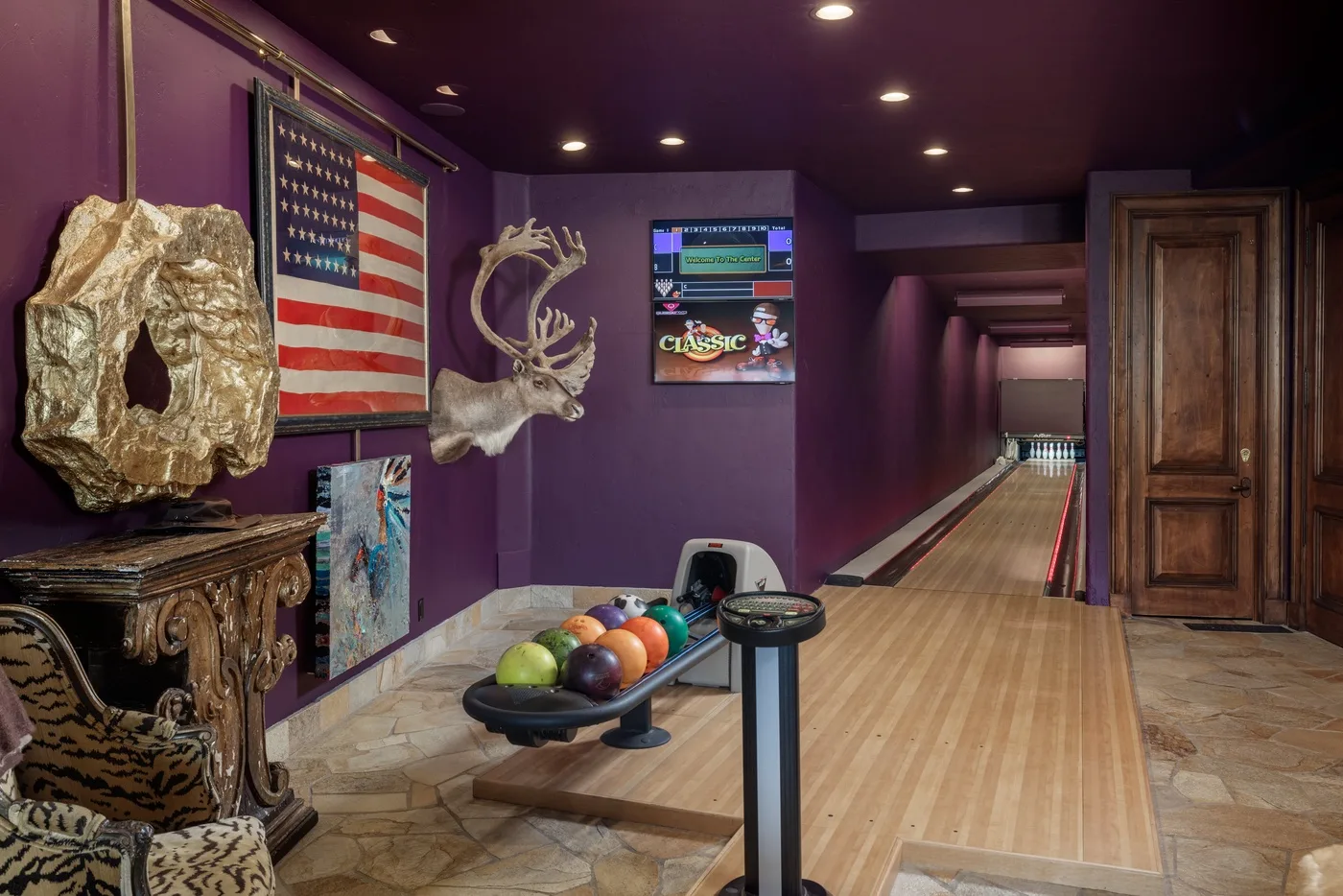 A bowling lane extends through a purple-walled room with a ball return.