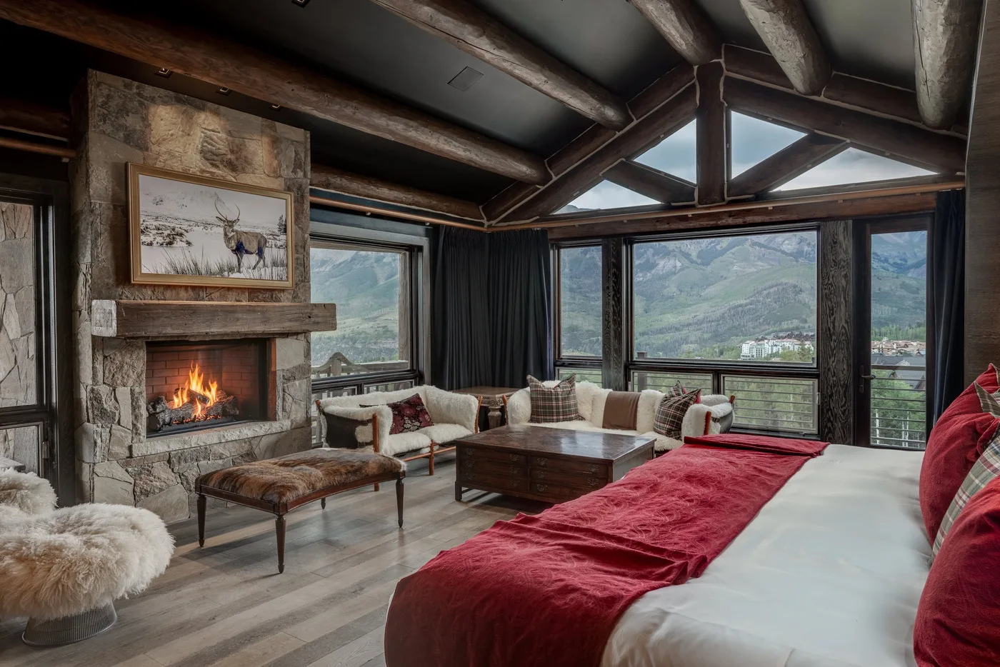 A mountain-view living room with a stone fireplace, seating, and a bed in the foreground.
