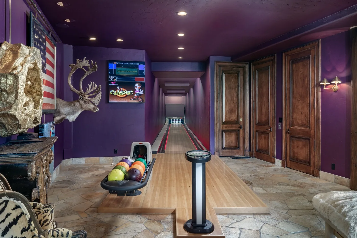A bowling alley with a ball return and wooden lanes in a purple room.