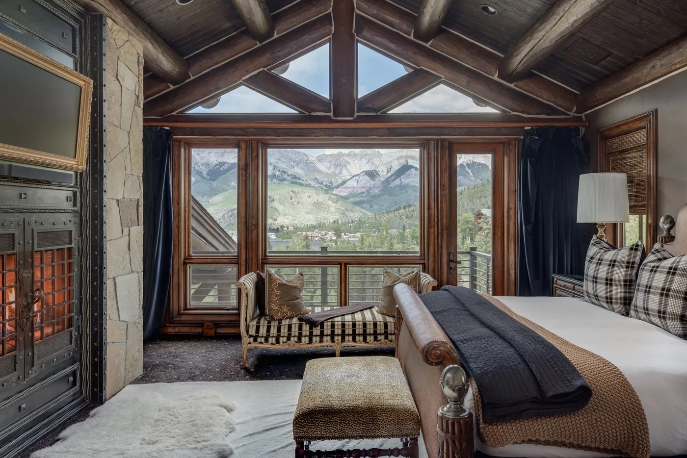 A bedroom with a bed and seating beside large windows overlooking a mountain valley.