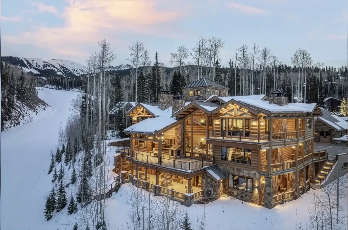 A large lodge glows beside a snowy forest and winding mountain road.