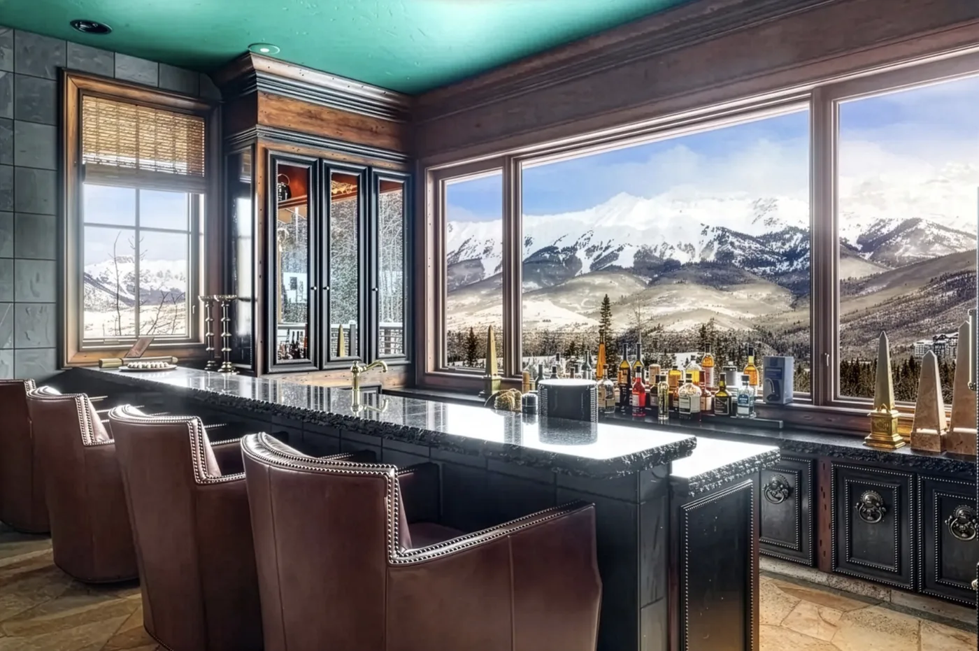 A dark bar with brown seating faces large windows overlooking snowy mountains.