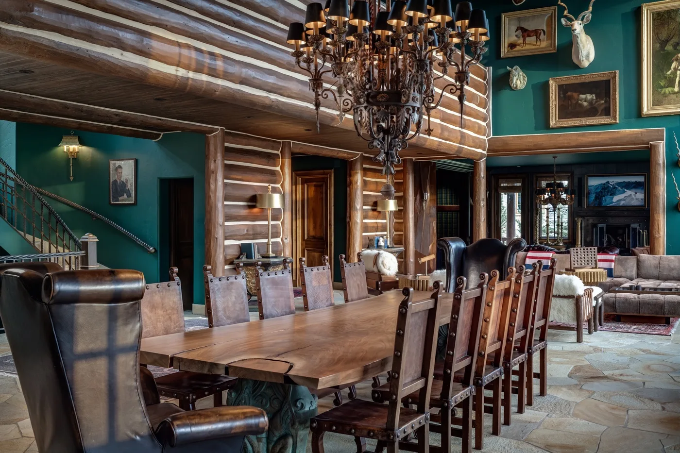 A rustic dining room with a long wooden table and chairs beneath a chandelier.