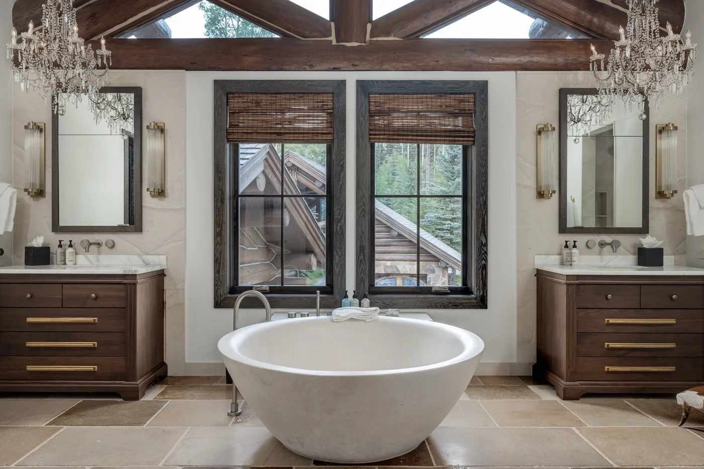 A bathroom with a freestanding bathtub, twin sinks, and windows beneath a timber ceiling.