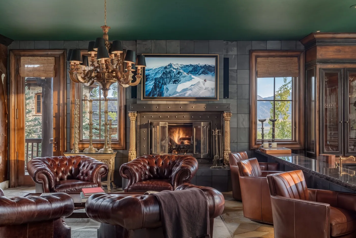 A paneled living room with leather seating and a fireplace beneath a mountain image.