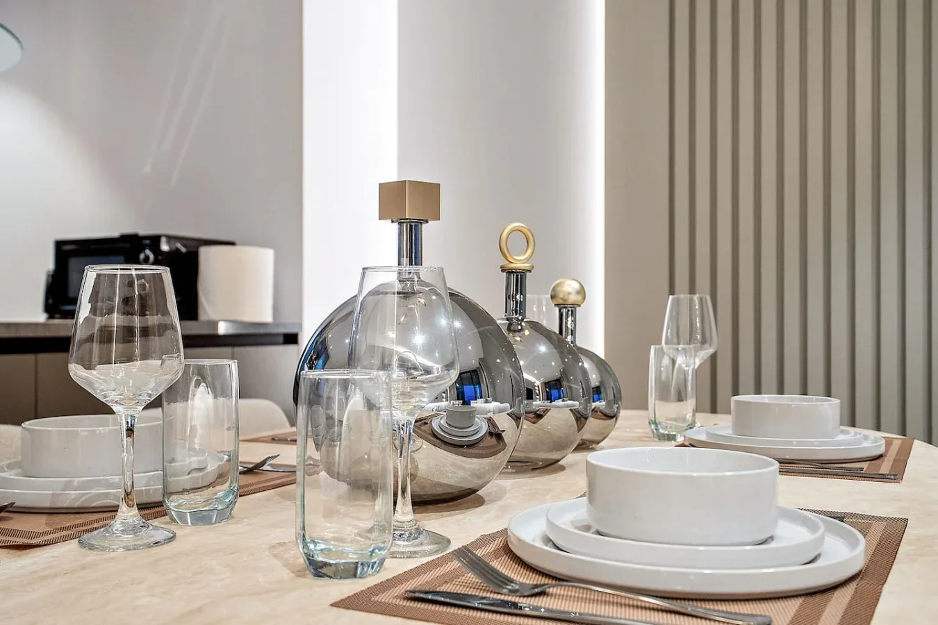 Una mesa de comedor está puesta con platos blancos, cristalería y botellas decorativas de vidrio.