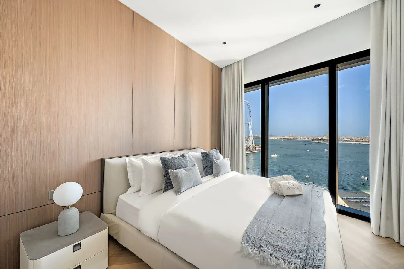 Un dormitorio con una cama bien hecha junto a grandes ventanales con vistas al agua.