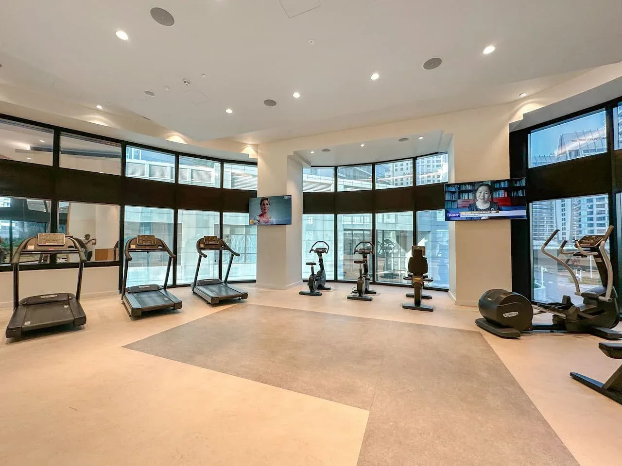 Un gimnasio con máquinas de ejercicio y grandes ventanas.