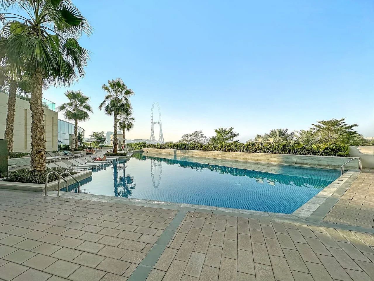 Una piscina al aire libre rodeada por una terraza pavimentada y palmeras.