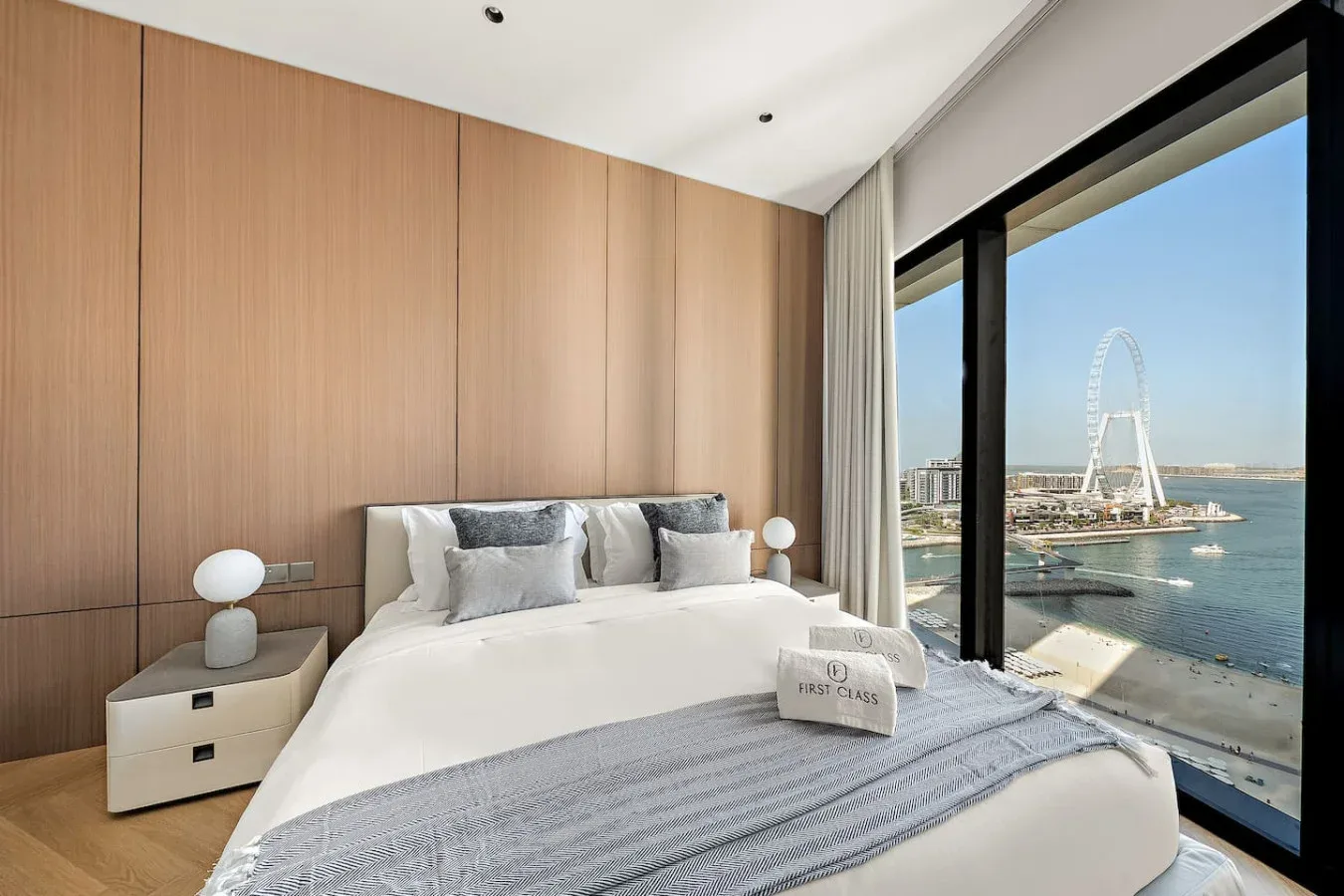 Un dormitorio con una cama bien arreglada junto a una gran ventana con vistas al agua.
