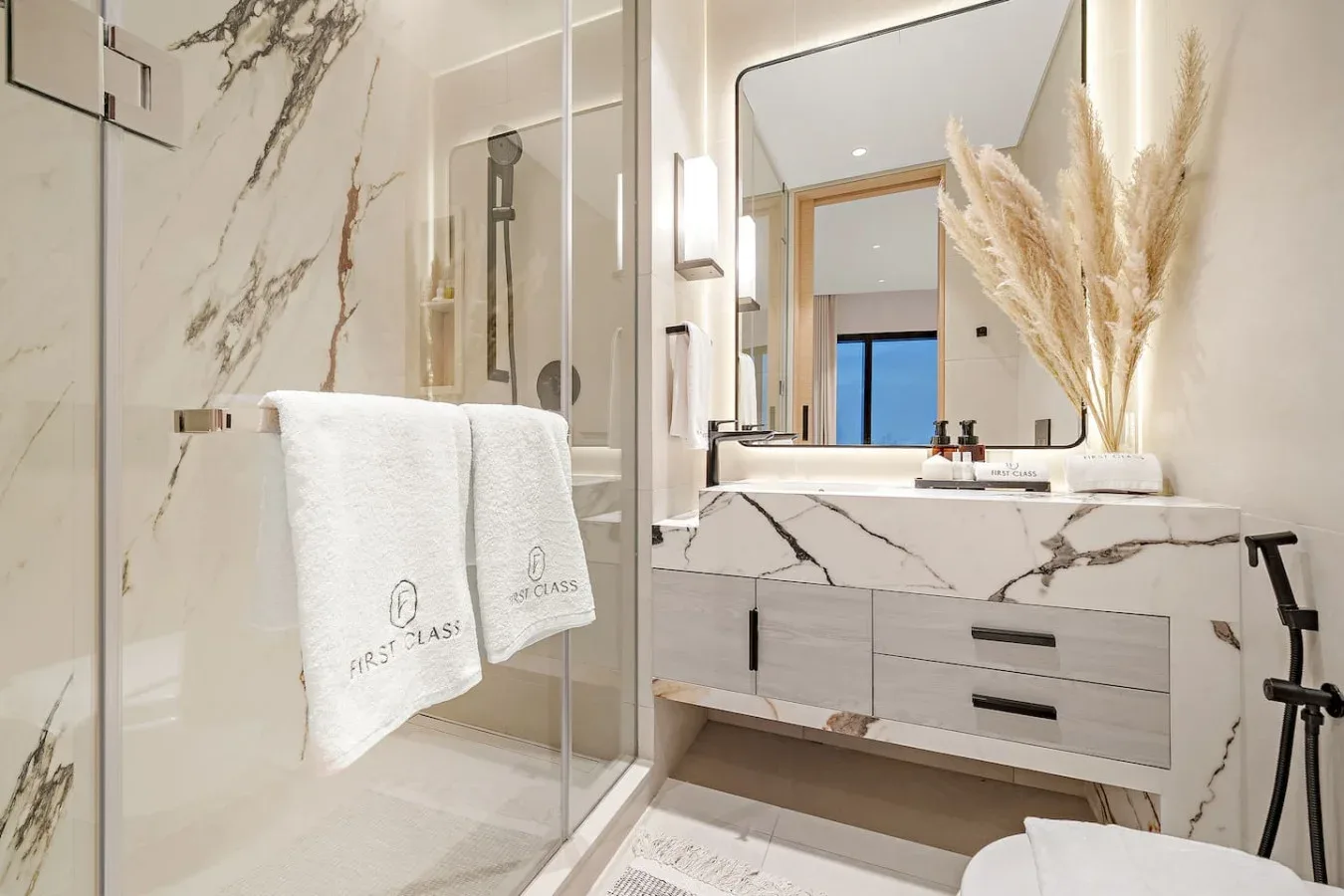 Un baño luminoso con ducha de vidrio y tocador con vetas decorativas.