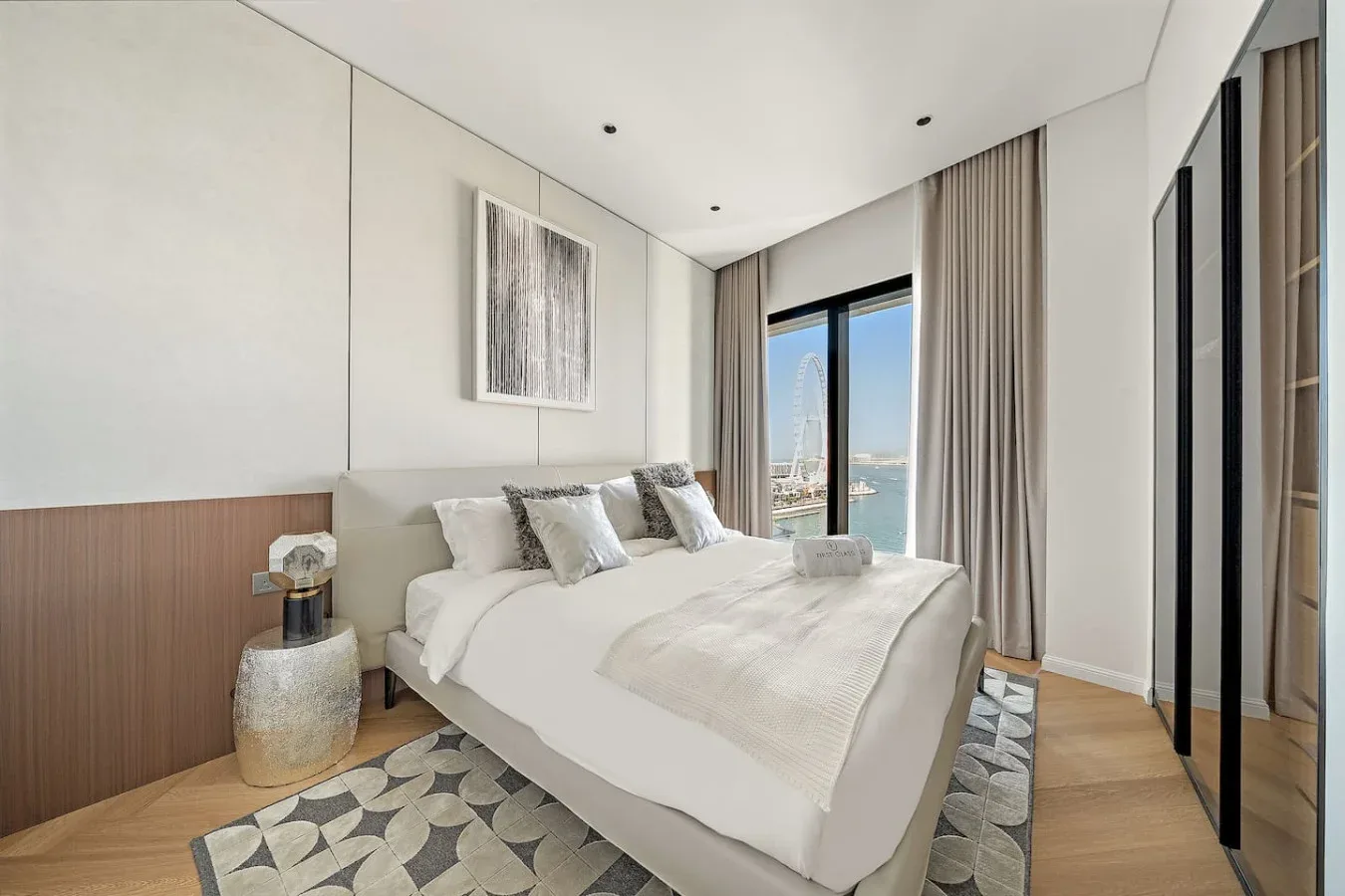 Un dormitorio luminoso con una cama bien tendida y ventanas altas con vistas al agua.