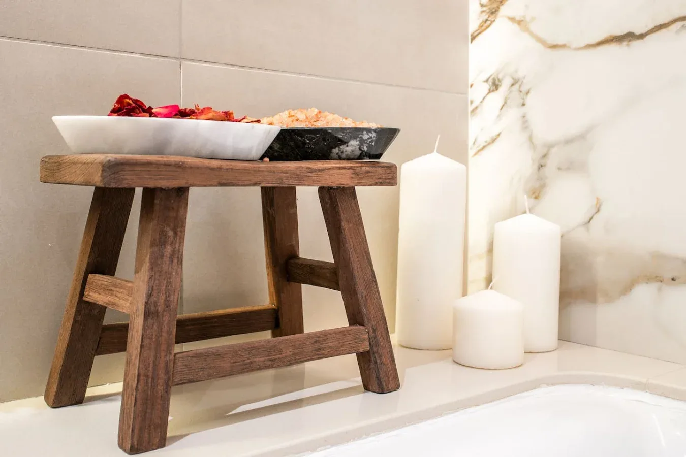 Un taburete de madera sostiene un plato junto a velas sobre una encimera de baño.