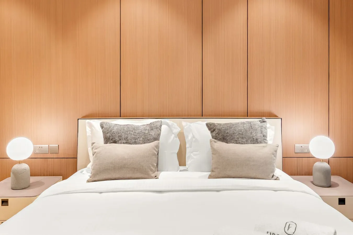 Una cama bien arreglada con varias almohadas está frente a una pared revestida de madera.