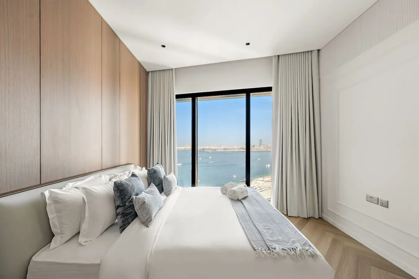 Un dormitorio luminoso con una cama tendida frente a una gran ventana con vistas al agua.