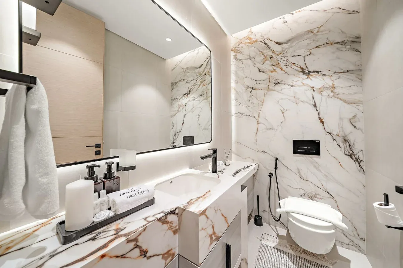 Un baño luminoso de mármol con lavabo, espejo e inodoro.