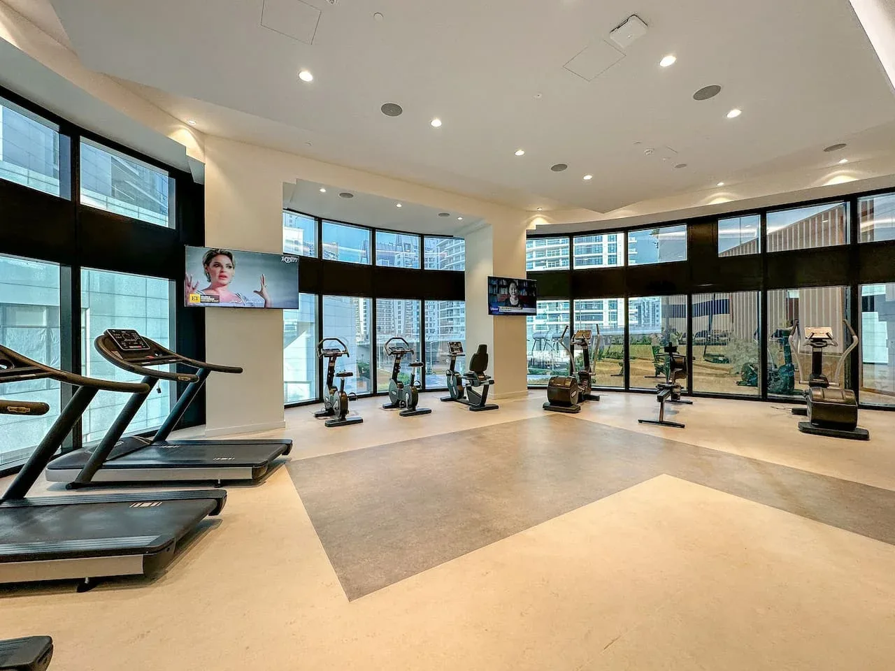 Un gimnasio luminoso con equipos de ejercicio junto a grandes ventanales.
